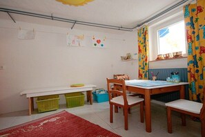 A room with a wooden table, chairs, a window with curtains, and children's artwork on the wall. - Holiday home with 4 bedrooms (Timmendorfer Strand)