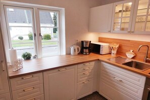 A kitchen with white cabinets, a wooden countertop, a coffee maker, a toaster, and a sink. - Holiday home with 4 bedrooms (Timmendorfer Strand)