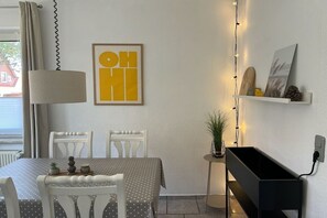 A dining area with a table set for two, a lamp, and a wall-mounted shelf with decorative items. - Holiday apartment with 2 bedrooms (Fehmarn)
