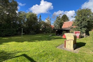 A well-maintained grassy yard with a small structure, possibly a shed, and a red-roofed building in the background. - Holiday apartment with 2 bedrooms (Fehmarn)