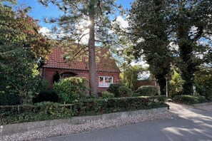 A brick house with a red-tiled roof, surrounded by dense greenery and a gravel driveway. - Holiday apartment with 2 bedrooms (Fehmarn)