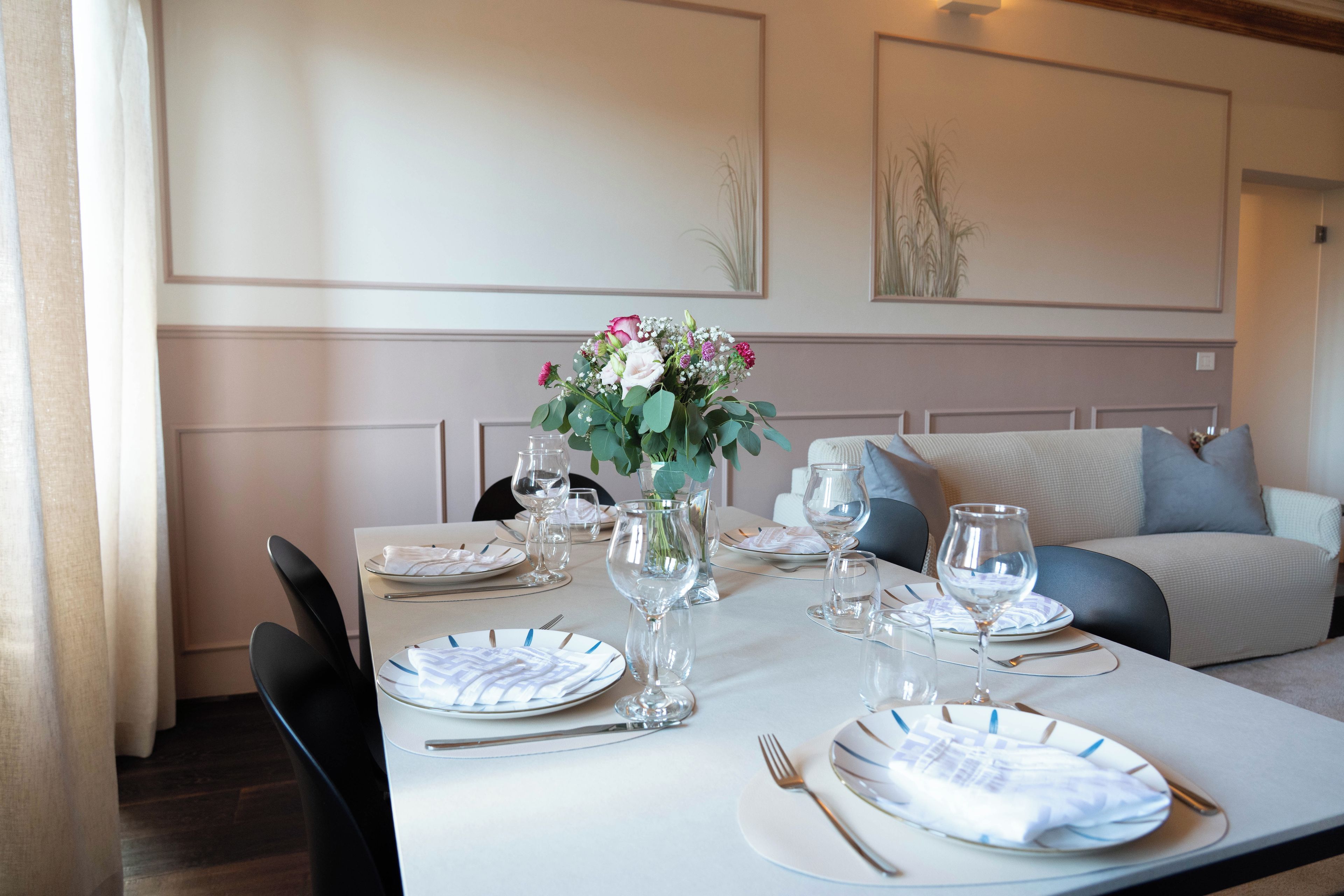 A dining table set with plates, cutlery, and glasses, with a vase of flowers in the center.