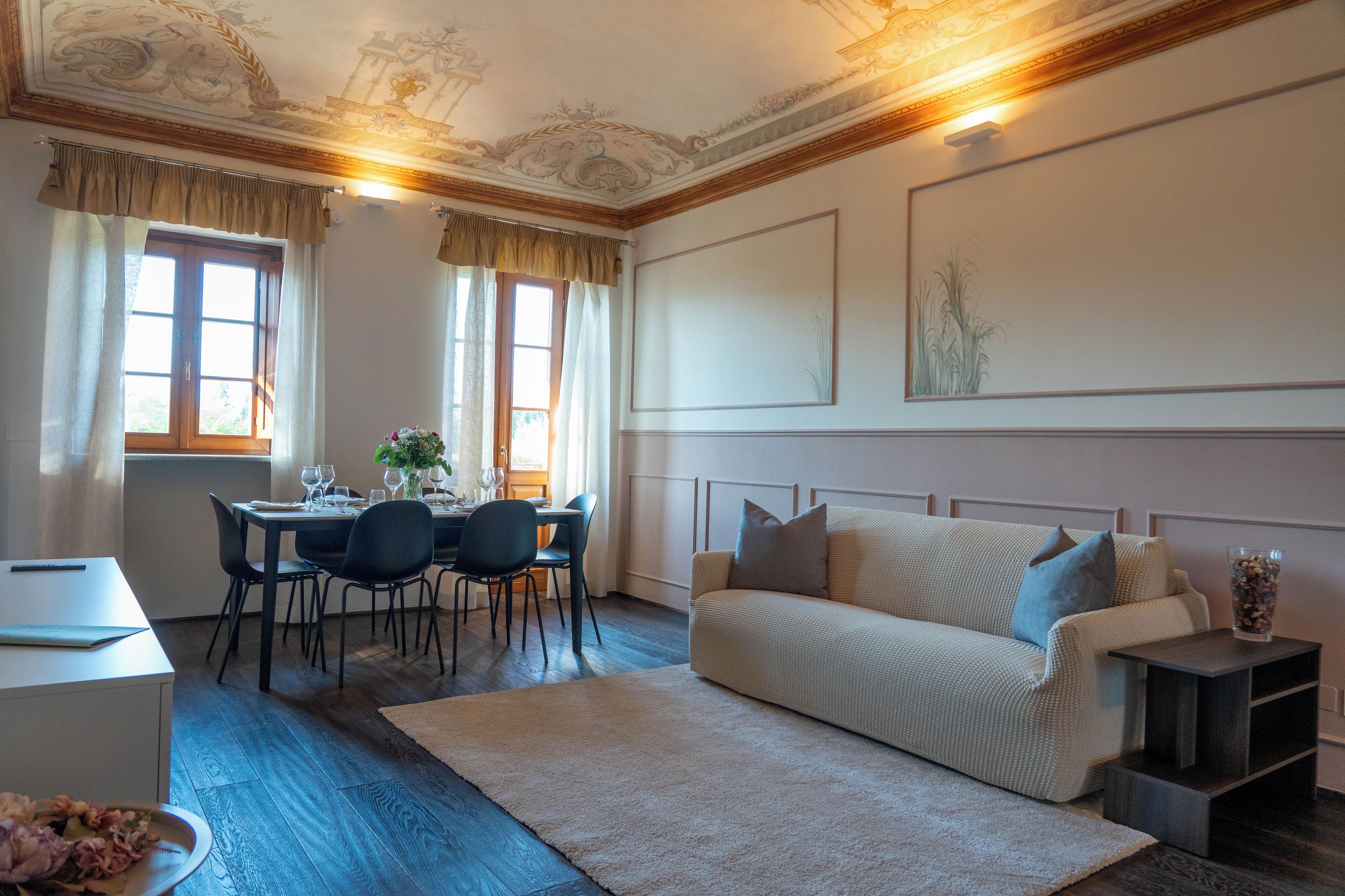 A room with a dining table set for four, a sofa, a small cabinet, and a decorative vase.