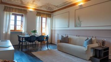A room with a dining table set for four, a sofa, a small cabinet, and a decorative vase.