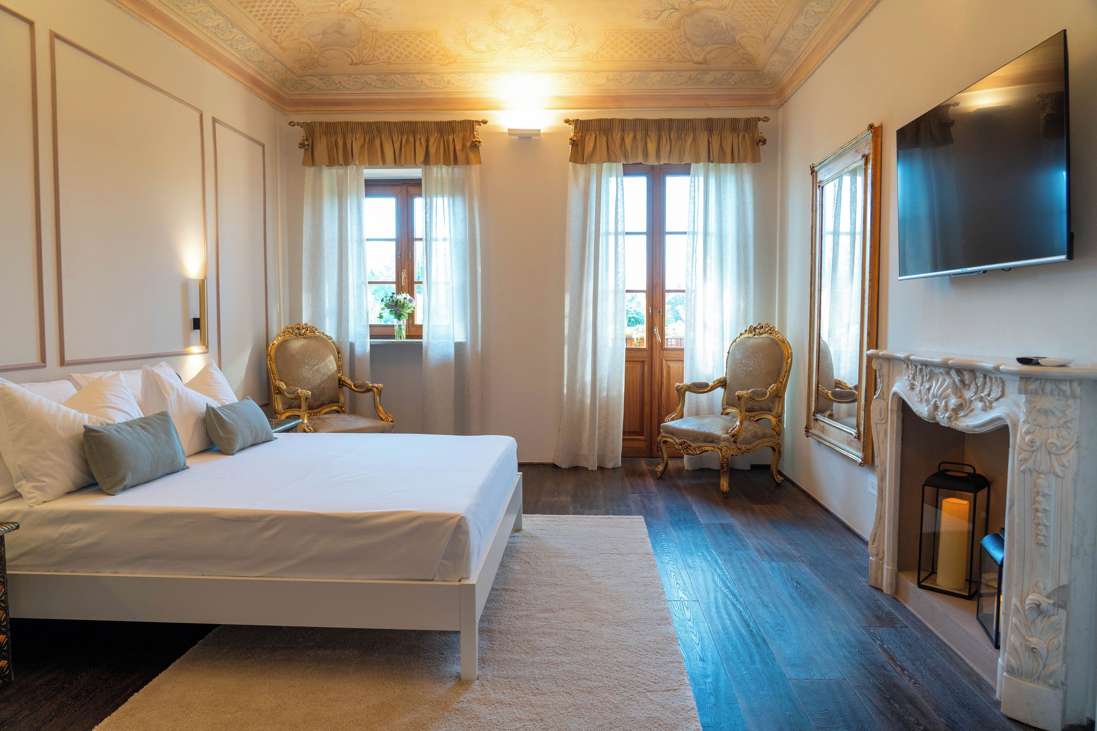 A hotel room with a large bed, two chairs, a fireplace, and a TV mounted on the wall.
