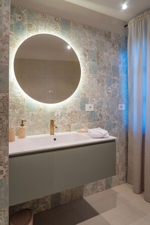 A bathroom with a large mirror, a sink, and a towel rack. - Rose Apartment (Piemonte)