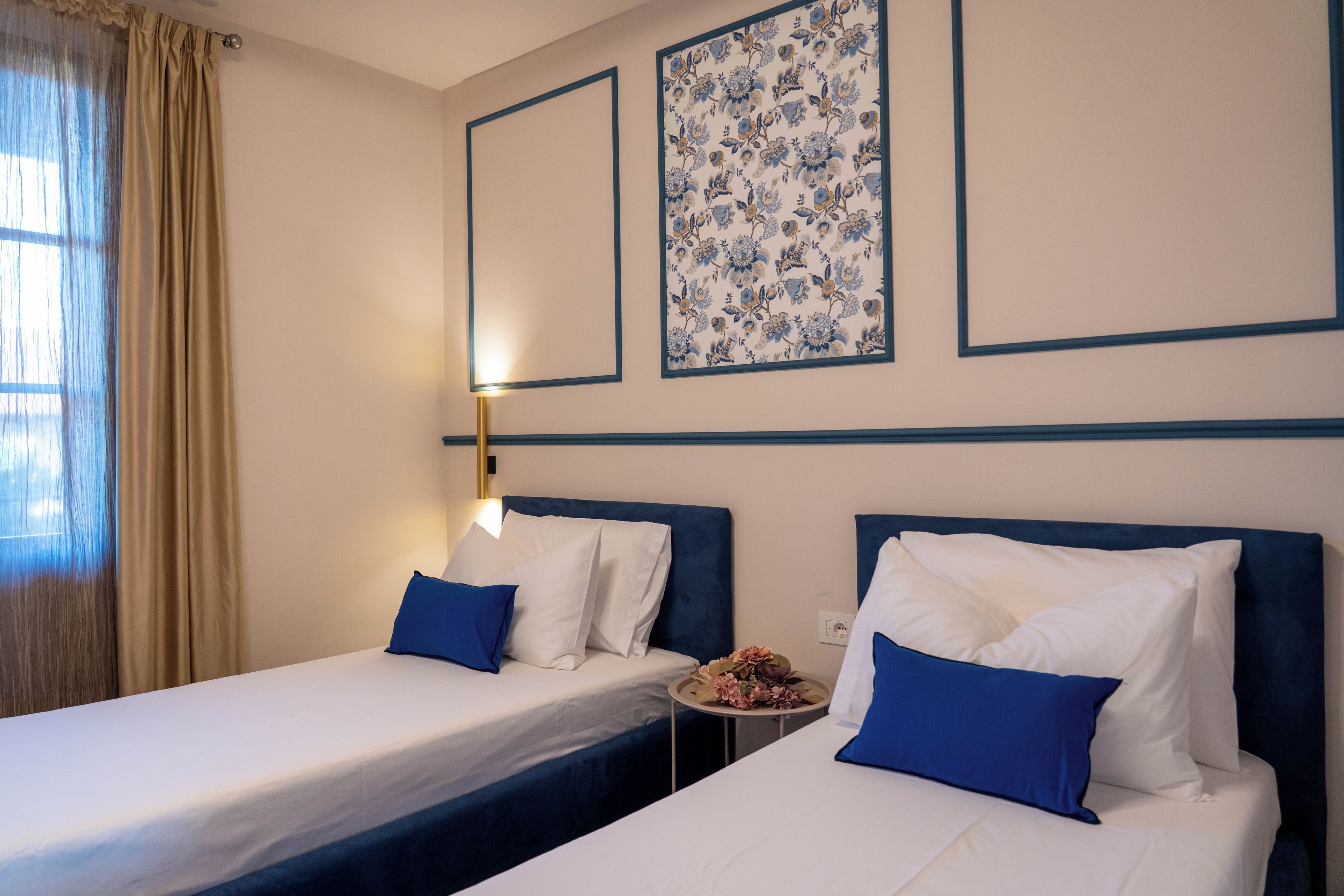A hotel room with two beds, a nightstand, a lamp, and a floral wall decoration.