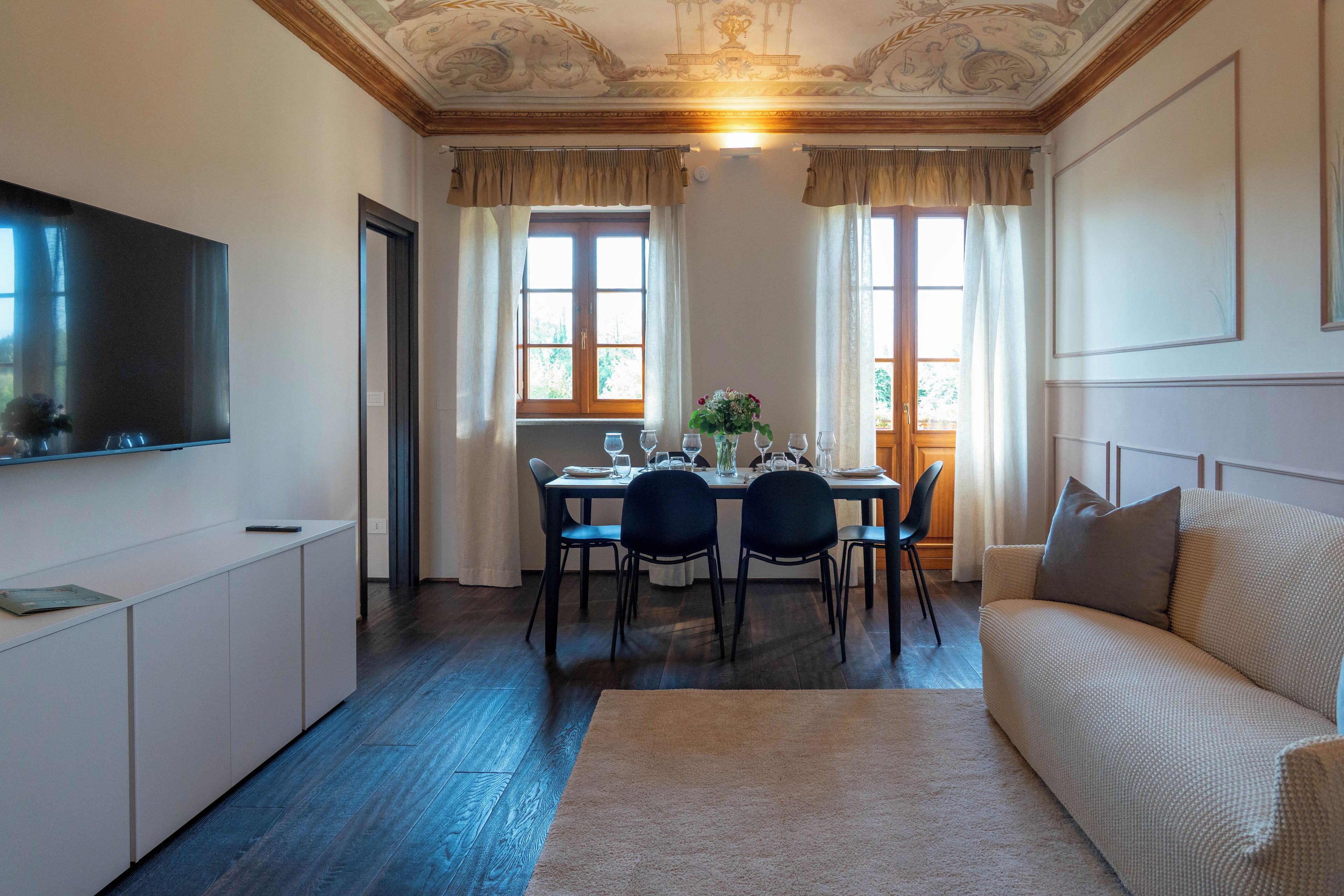 A dining area with a table set for four, a sofa, and a television on the wall.