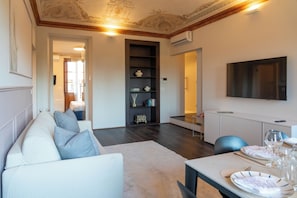 A modern living room with a sofa, a dining table set for two, and a flat-screen TV mounted on the wall. - Rose Apartment (Piemonte)