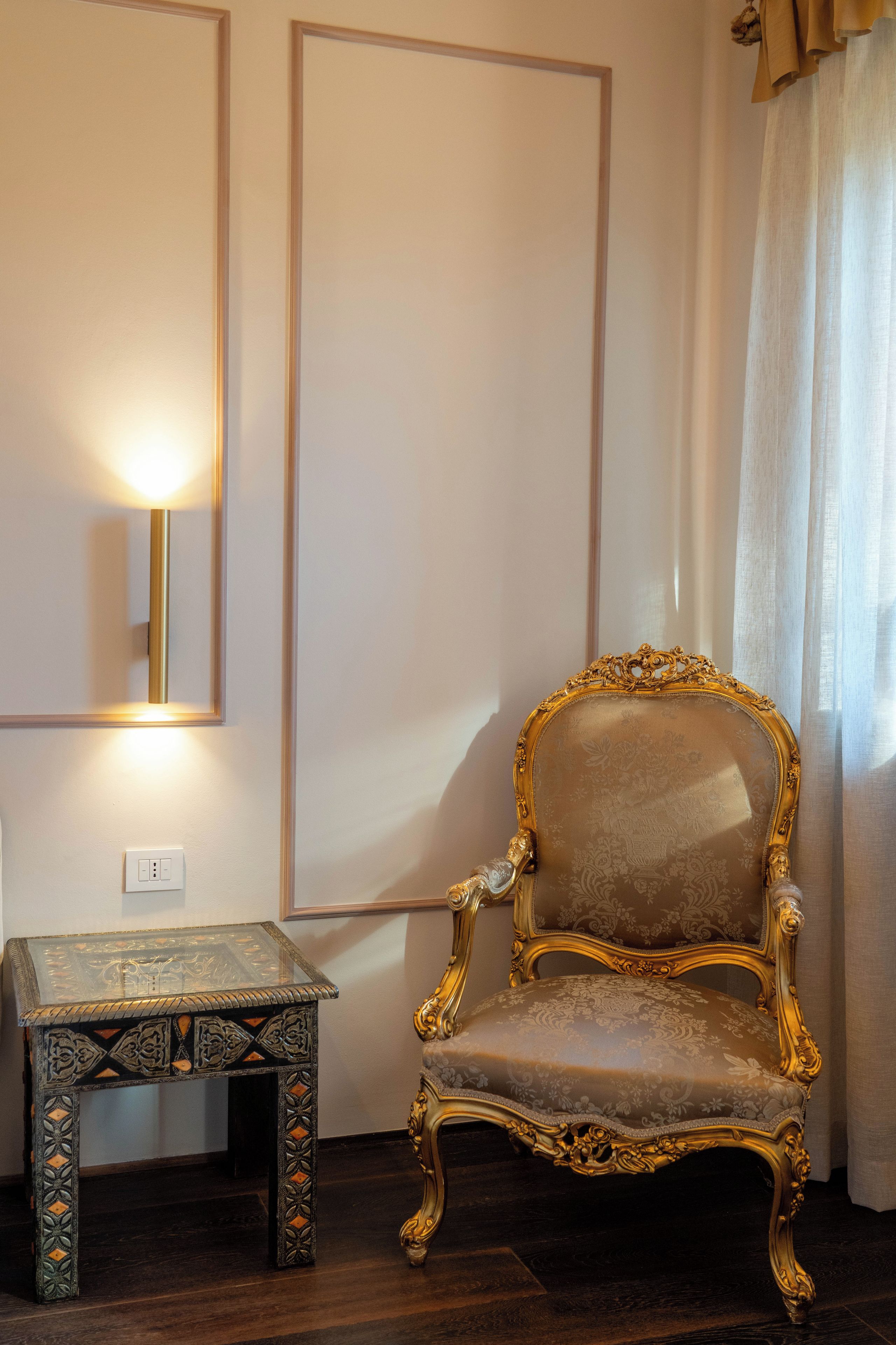 A room with a large mirror, a decorative chair, and a small table with intricate designs.