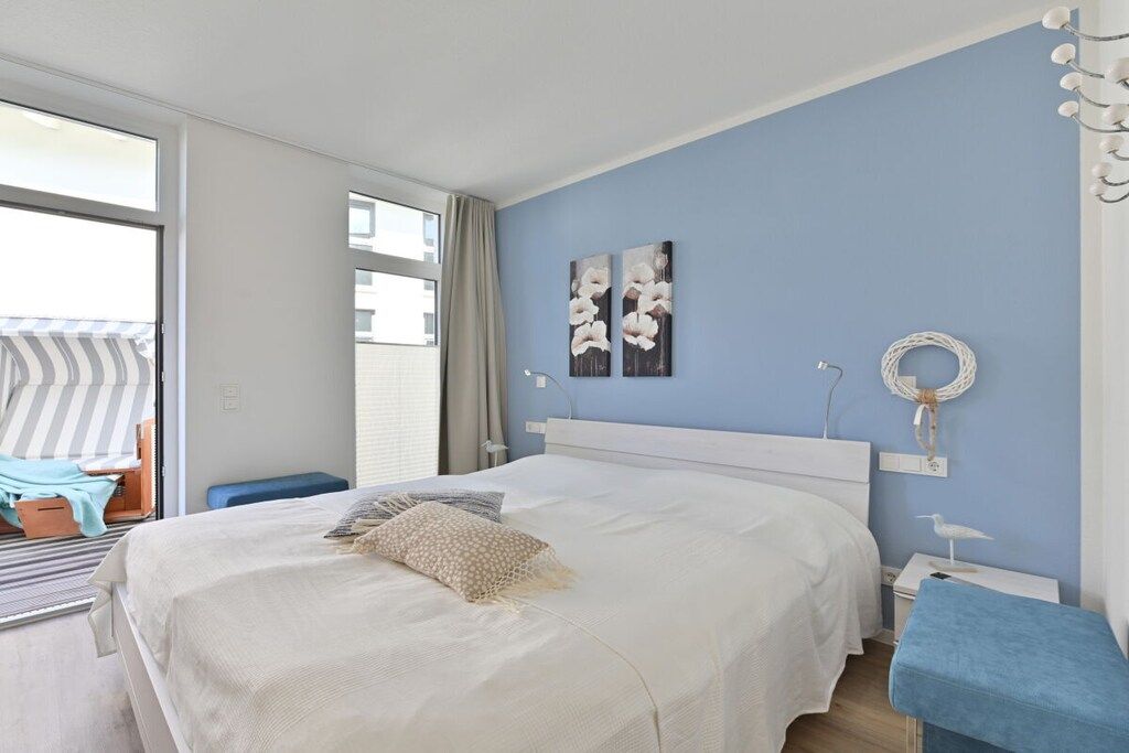 A bedroom with a large bed, a bedside table, a chair, and a view through a sliding door.