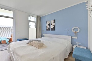 Ein Schlafzimmer mit einem großen Bett, einem Nachttisch, einem Sessel und Blick durch eine Schiebetür.