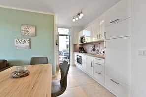 Una cucina moderna con mobili bianchi, un tavolo da pranzo in legno e due opere d'arte appese al muro.