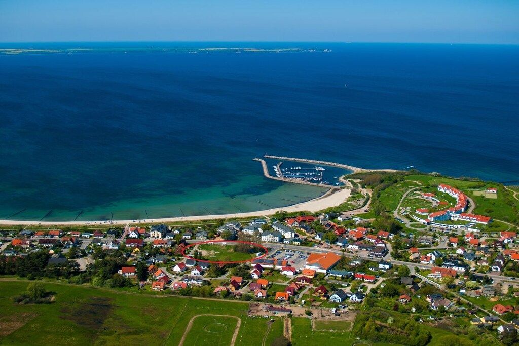 An aerial view of a coastal town with a beach, houses, and a marina.