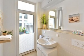 Ein modernes Badezimmer mit einem großen Fenster, einem Waschbecken und einem Spiegel.