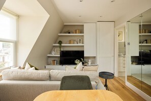 A modern living room with a sofa, a dining table, and a TV. - The Two-Bedroom Edit (London)