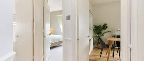 A hallway leading to a bedroom with a bed, a small table, and a potted plant.