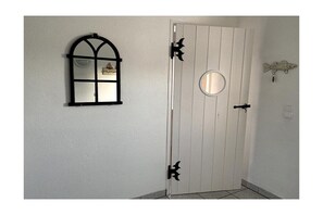 Une porte blanche ornée d’un miroir rond et d’une fenêtre à cadre noir.