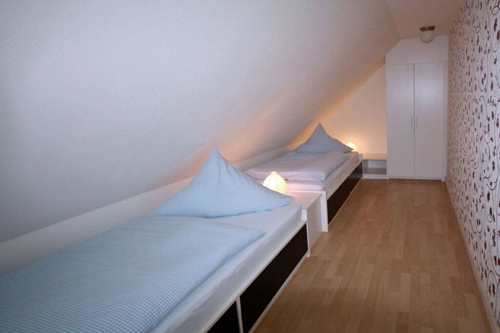 Ein kleiner, schmaler Raum mit zwei Einzelbetten nebeneinander an der Wand, einem weißen Kleiderschrank und einem Wandbehang mit Muster auf einer Seite.