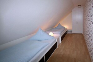 A small, narrow room with two single beds aligned against the wall, a white wardrobe, and a patterned wallpaper on one side. - Holiday apartment with 2 bedrooms (Utersum auf Föhr)