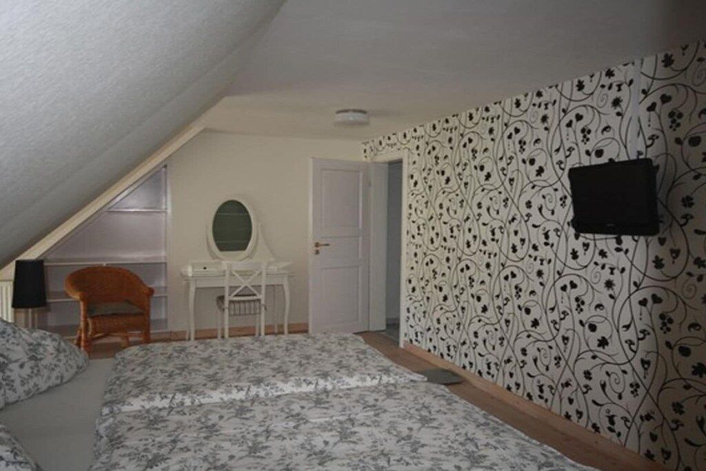 Un dormitorio con techo inclinado, cama con ropa de cama floral, escritorio con espejo y pared estampada.