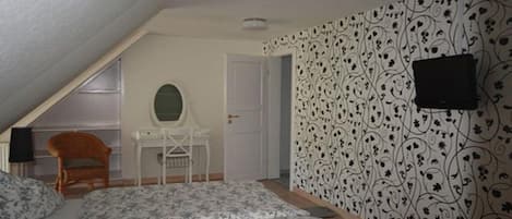 Un dormitorio con techo inclinado, cama con ropa de cama floral, escritorio con espejo y pared estampada.