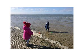 Zwei Kinder spielen am Strand, im Hintergrund das Meer.