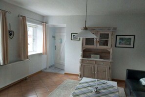Une pièce avec un radiateur, une table avec un set de table, un luminaire suspendu, un meuble et une porte donnant sur une autre pièce.