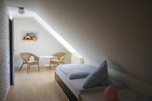 Ein kleiner, gemütlicher Raum mit einem Bett, zwei Stühlen, einem Tisch und einem Bild an der Wand.