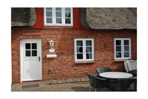 A brick building with a white door, two windows, and a table with chairs outside. - Holiday apartment with 2 bedrooms (Utersum auf Föhr)