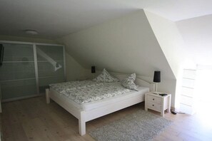 A bedroom with a bed, bedside tables, a nightstand, a window, and a door. - Holiday apartment with 2 bedrooms (Utersum auf Föhr)