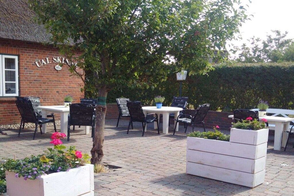 An outdoor seating area with tables and chairs, a brick building with a sign, and potted plants.