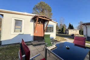 Una piccola casa con un patio, una porta in legno e un tavolo con sedie.