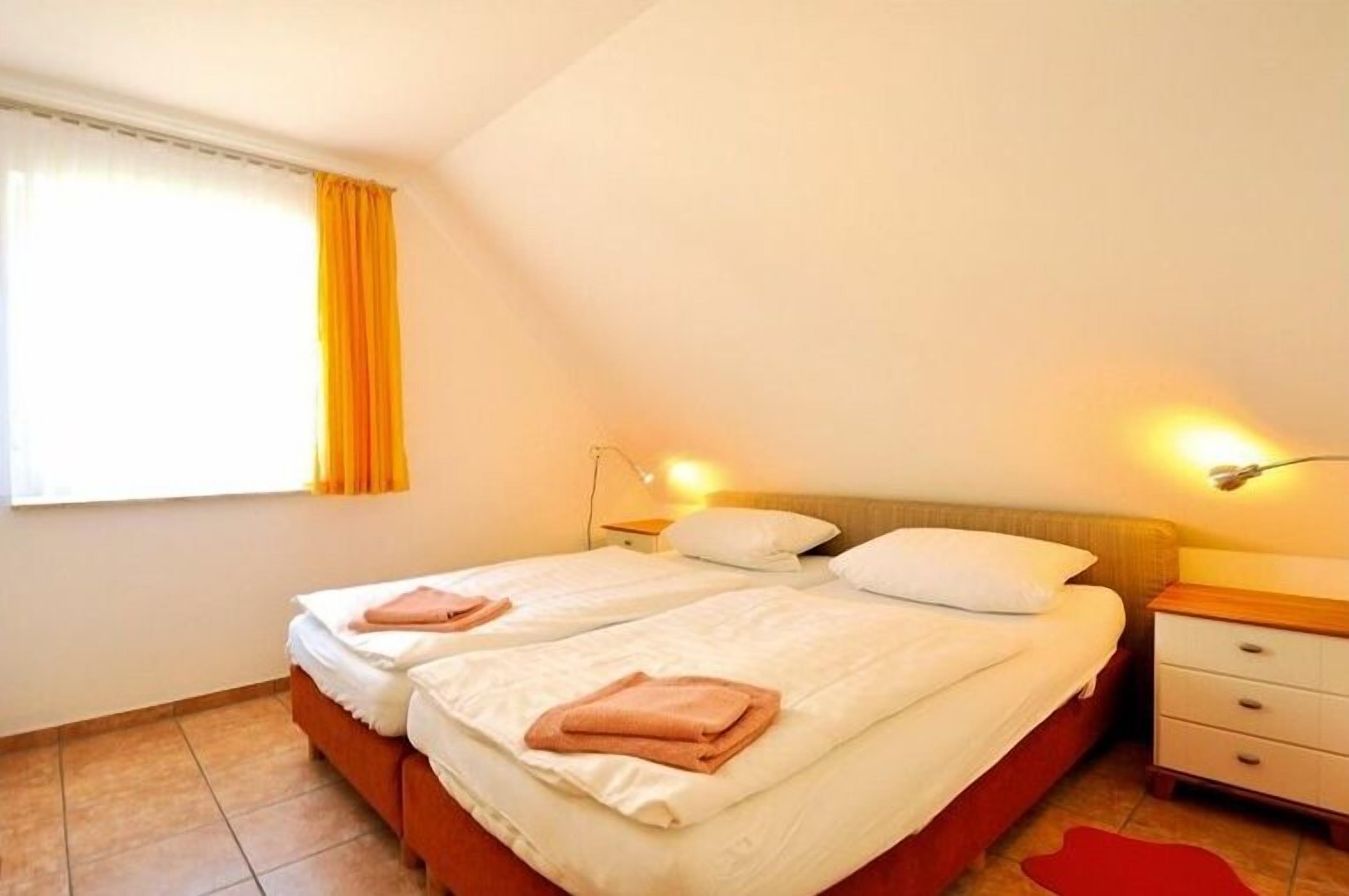 Ein Zimmer mit zwei Betten, einem Nachttisch und einem Fenster mit Vorhängen.