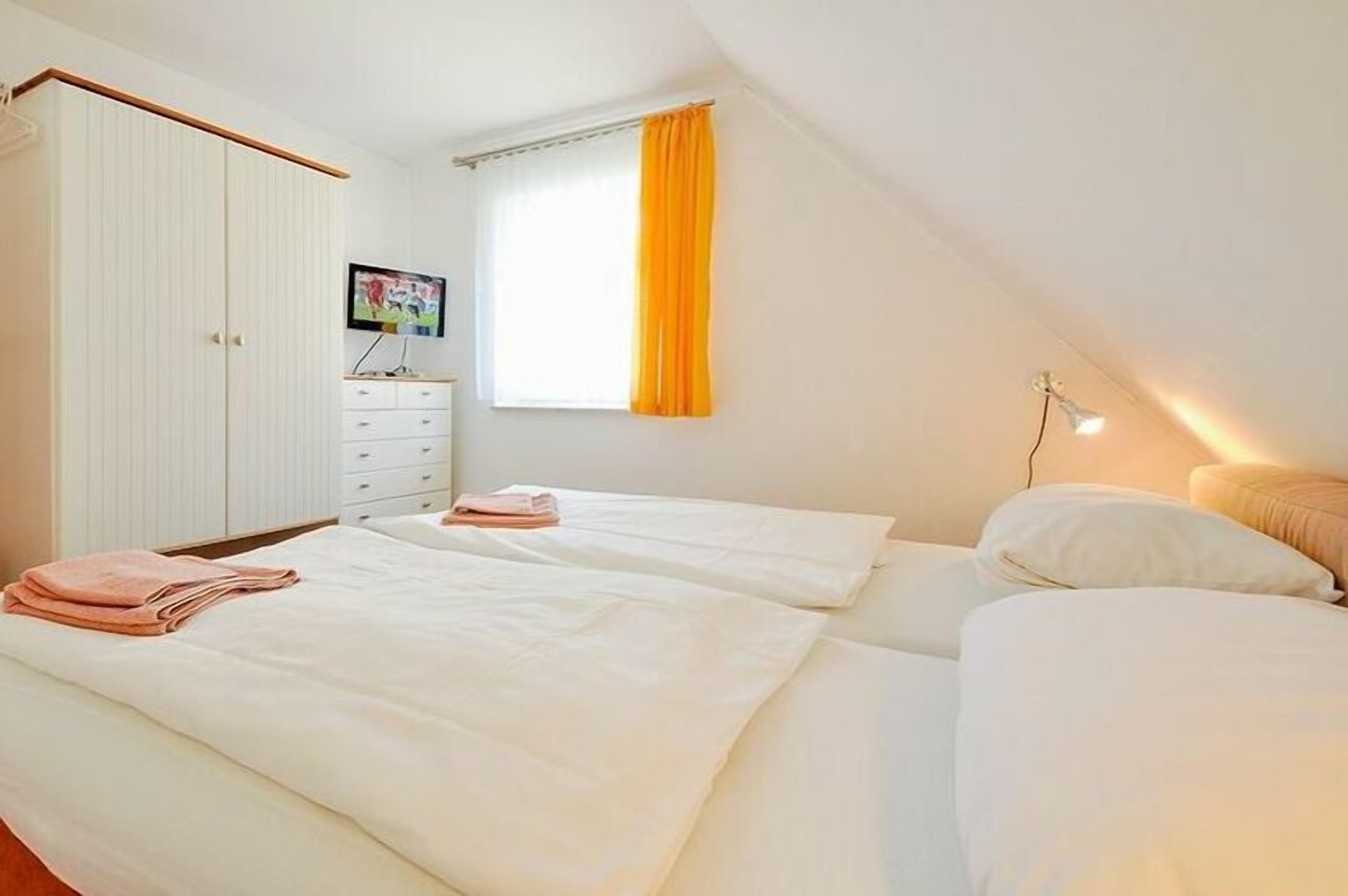 A bedroom with two beds, a wardrobe, a television, and a window with curtains.