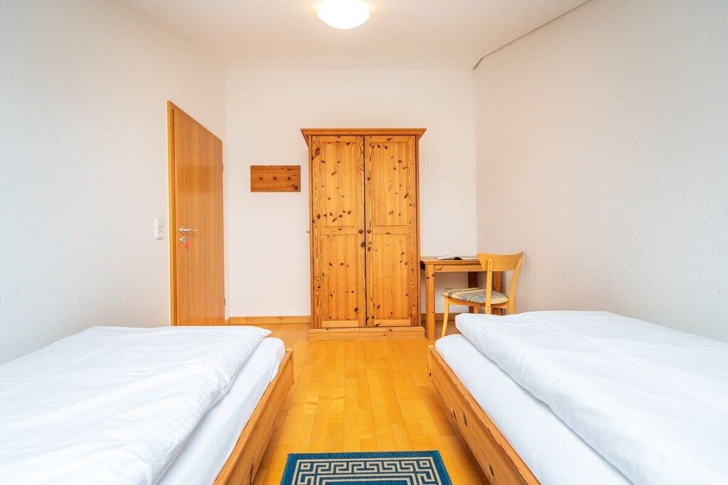 Une chambre avec deux lits, une armoire en bois, un bureau et une chaise.