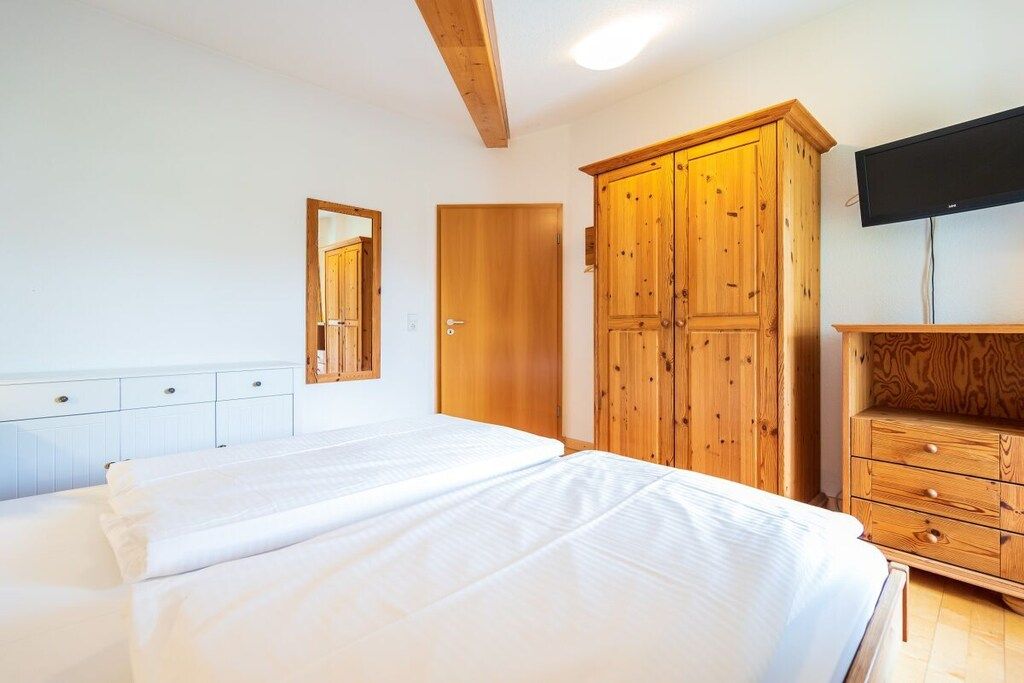 Un dormitorio con cama, armario de madera, televisión y espejo.