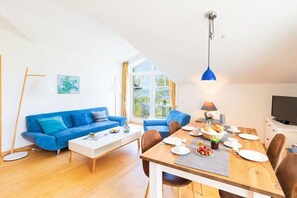 Ein modernes Wohnzimmer mit einem blauen Sofagarnitur, einem Holzessttisch mit Stühlen und einem Fernseher.