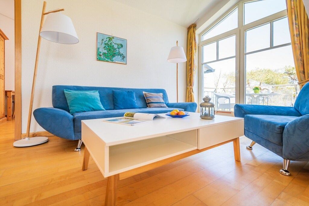 A modern living room with a blue sofa, a white coffee table, and a large window with curtains.