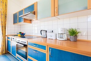 A kitchen with blue cabinets, a stainless steel range hood, a toaster, a coffee maker, and a potted plant. - Holiday apartment with 2 bedrooms (Juliusruh)