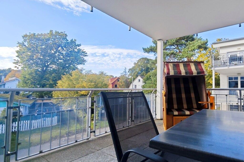 Ein Balkon mit Tisch und Stühlen, ein gestreifter Markise und Blick auf Bäume und Gebäude.