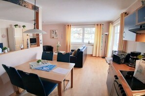 A compact living space with a dining area, kitchenette, and a sofa. - Holiday apartment with 1 bedroom (Juliusruh)