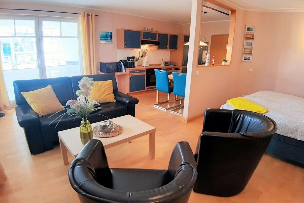 A compact living space with a sofa, a dining table, a kitchen area, and a bed.