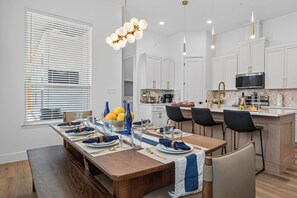 A modern kitchen with white cabinets, a central island, and a dining area set for six. - New Spacious Cowboys Retreat | Walk to AT&T Stadium (Arlington)