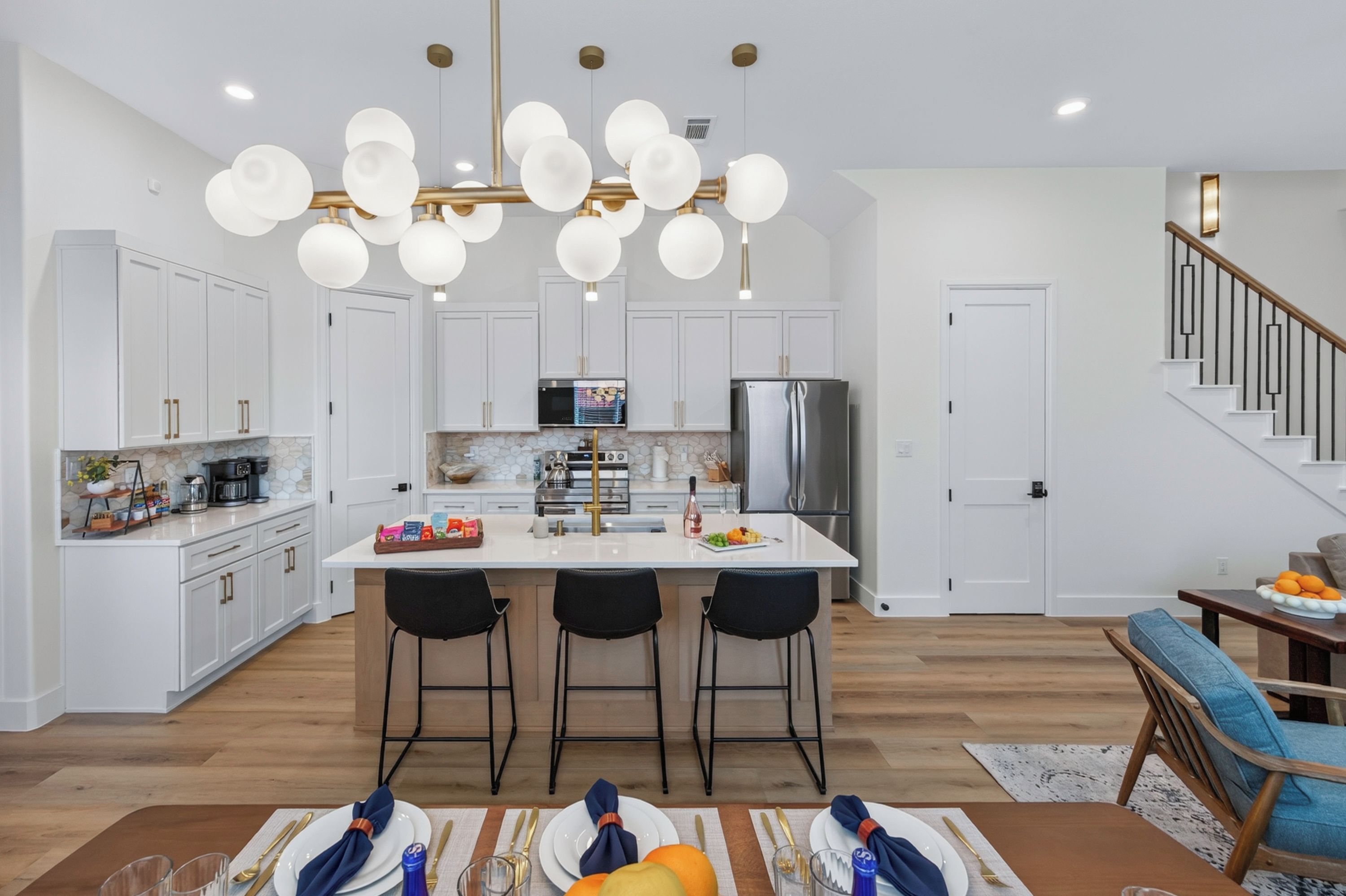 Una cocina moderna con armarios blancos, una isla central con taburetes de bar, un refrigerador de acero inoxidable y una lámpara colgante.