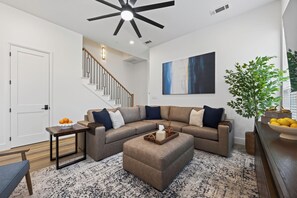A modern living room with a sectional sofa, ottoman, and a staircase leading to another level. - New Spacious Cowboys Retreat | Walk to AT&T Stadium (Arlington)