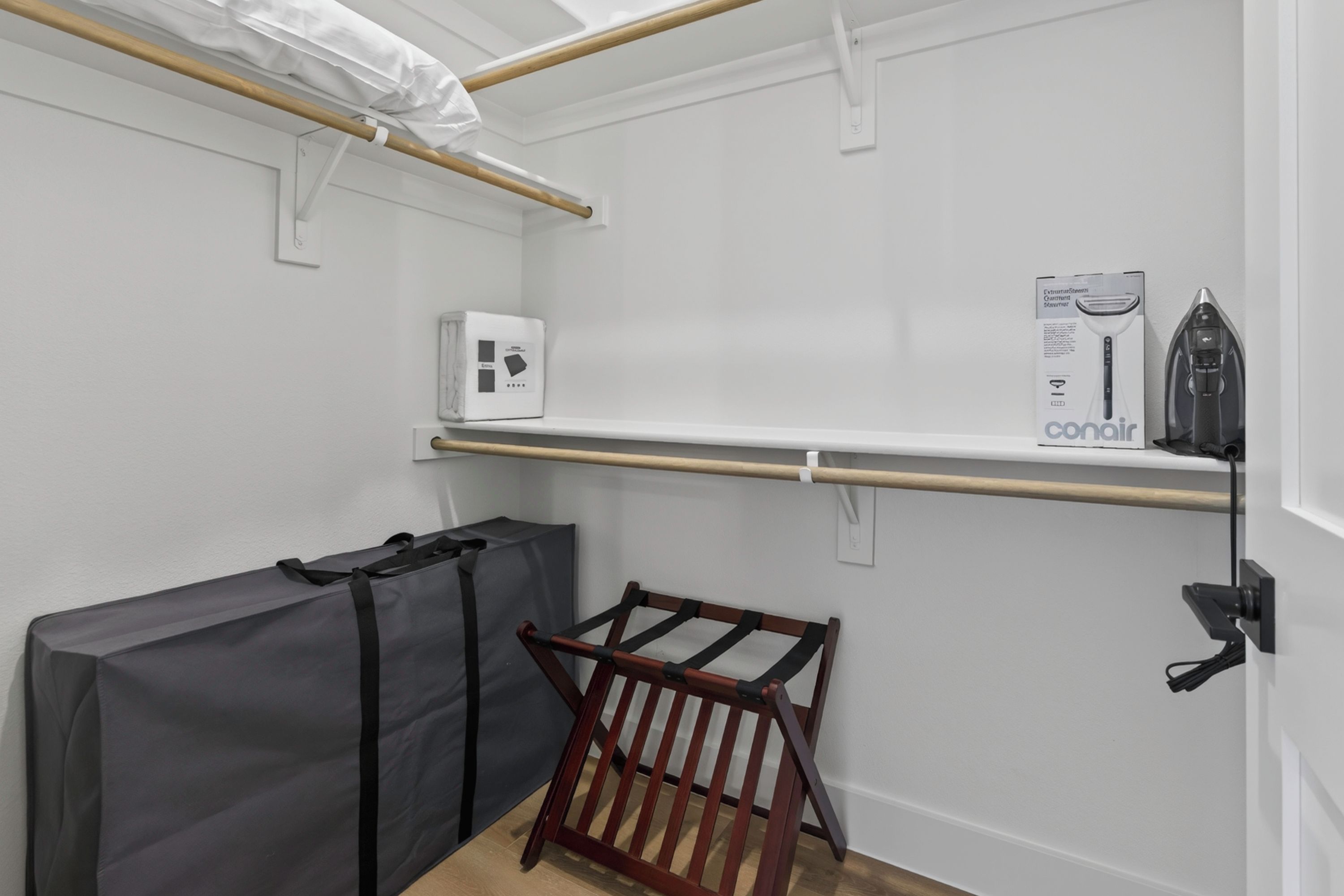 A compact room with a wooden floor, a small wooden chair, a black bag, a white box, and a shelf with a black object.