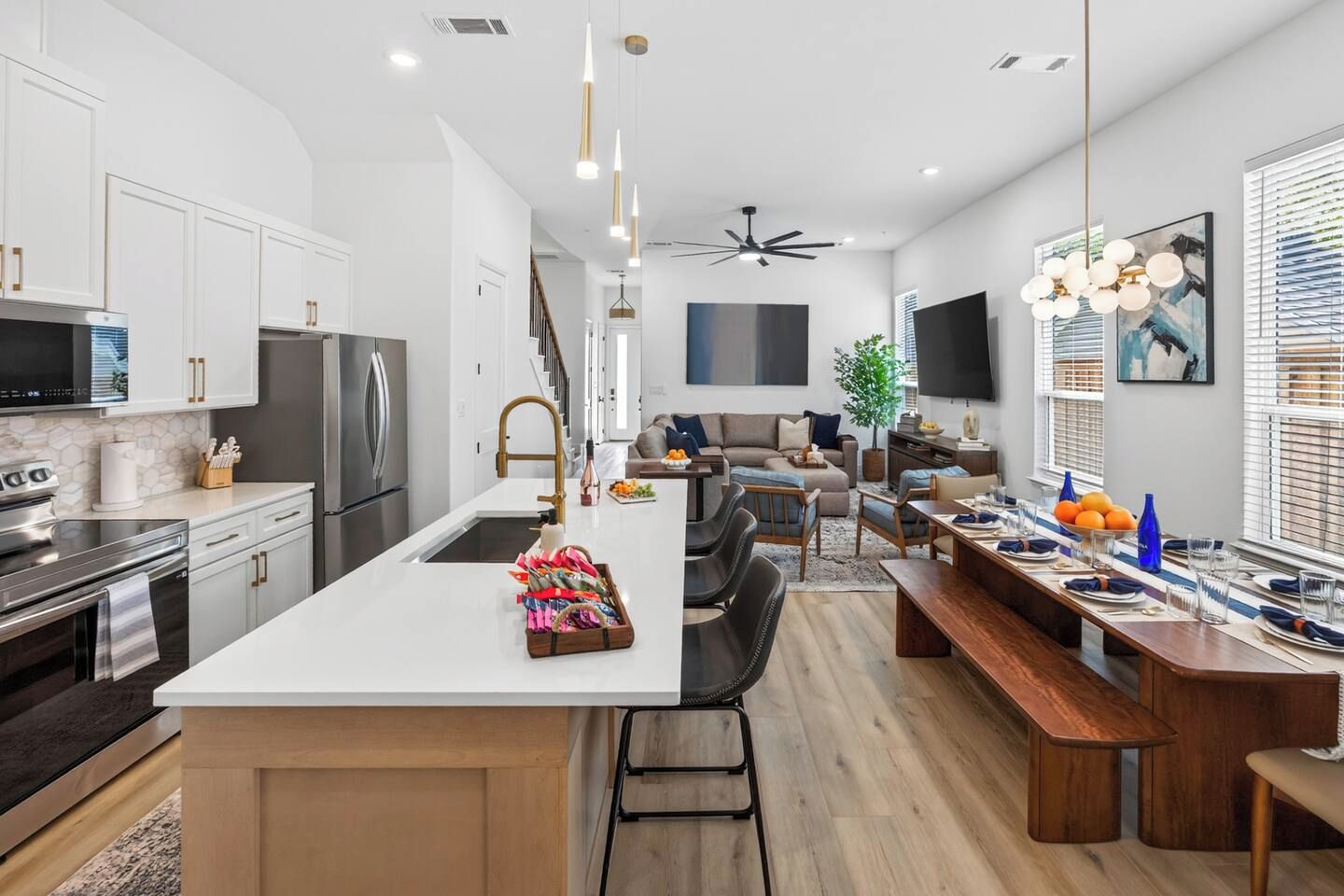 A modern kitchen with a central island, stainless steel appliances, and a dining area with a long table and benches.