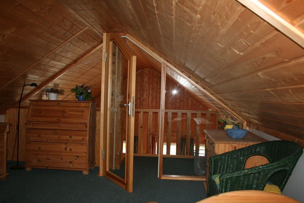 A wooden attic room with a sliding door, a dresser, a chair, and a small table with a bowl.