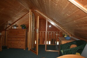 Ein hölzerner Dachbodenraum mit einer Schiebetür, einem Schrank, einem Stuhl und einem kleinen Tisch mit einer Schüssel.